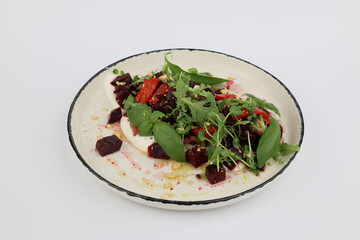 Baked beetroot salad with cheese and greens on a beautiful white plate on a white background