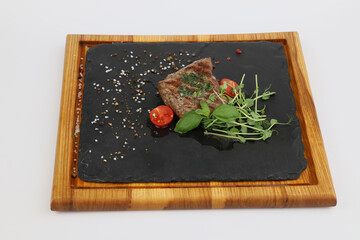 Filet Mignon steak with tomato and greens on a wooden board on a white background