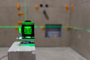 Glowing green laser spirit level built on a brick at a construction site with green lines. Accurate...