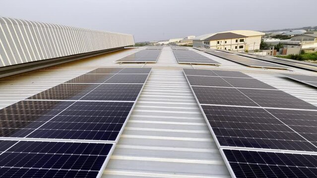 Rooftop Solar Array: Rows of photovoltaic solar panels gleam on the corrugated metal roof of an industrial building, symbolizing clean energy and sustainability under a hazy sky.