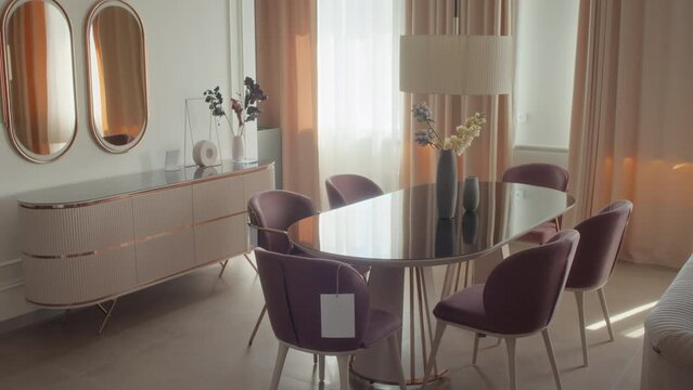 Interior of living room in minimalism with glass dining table, purple chairs, two big oval mirrors and peach-coloured cupboard
