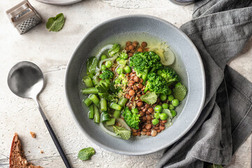Vegetarian minestrone soup with green vegetables and lentils in gray plate on textured background,...