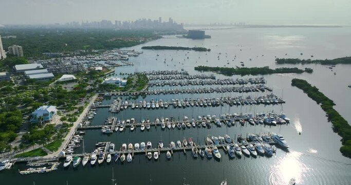 View from above of Dinner Key marina and Biscayne Bay in Coconut Grove upscale neighborhood with many expensive yachts and motorboats. High-rise buildings in downtown of Miami city in Florida, USA