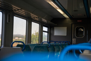Inside of a train car, which appears to be empty at this time. This tranquil scene is dominated by rows of blue and white seats arranged along the sides of the car. The train car is brightly lit.