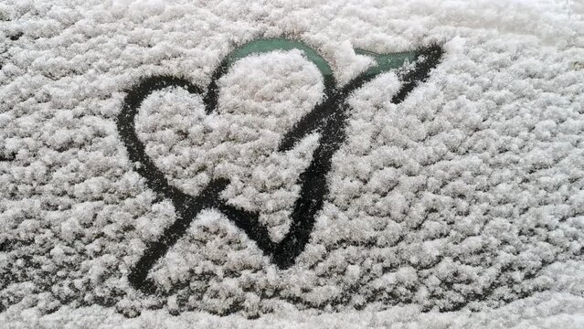 a finger-drawn heart on white snow on a car glass in cloudy weather