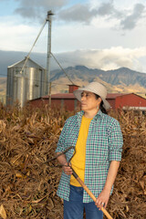Mujer empoderada al atardecer parada frente a una pila de hojas secas de maiz listas para el ganado, granjera cuidadonde de su granja empoderamiento femenino  - obrazy, fototapety, plakaty