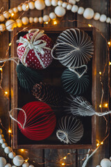 Cozy atmospheric photo, home festive atmosphere. Collection of old fashioned christmas new year foldable honeycomb toys, craft holiday decoration in vintage wooden box. Magic lights on background