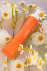 Orange cosmetic tube and chamomile flowers