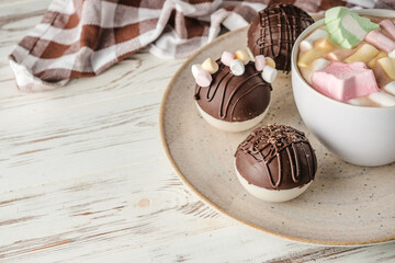 Chocolate bomb with cocoa powder and mini marshmallow to prepare a fragrant hot drink. On white wooden background.