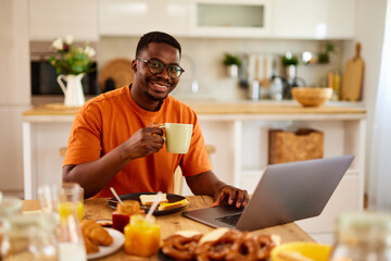African American man using laptop while enjoying breakfast  at home