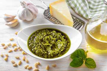 Homemade pesto sauce in small jar and ingredients for pasta on white wooden background with copy space. Traditional Italian cuisine, recipe, restaurant menu