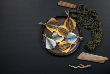a plate of dried fish on a black background. Top view on a black background with an eco shopper.
