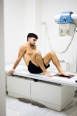 Vertical photo of a young man standing in a hospital ward undergoing an x-ray test on his foot....