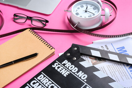 Notebook with movie clapper, film reel and alarm clock on pink background