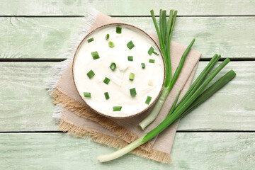 Fototapeta na wymiar Bowl of delicious sour cream with green onion on light wooden background