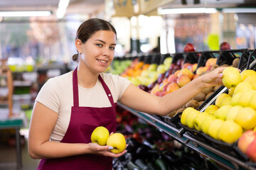 Positive female supermarket salesperson setting out apples on shelves