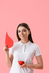 Female donor with paper blood drop and heart on pink background
