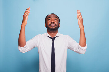 Worried black businessman is praying and raising his hands in a humble gesture towards the sky....