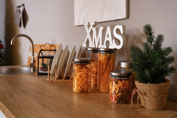 Wooden countertop with small fir tree, jars, plate rack and Christmas decor, closeup
