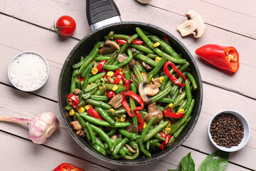 Frying pan with different vegetables on light wooden background