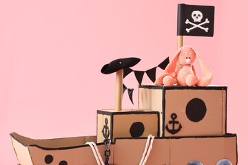 Pirate cardboard ship with toy bunny on pink background