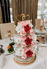 Obraz na płótnie Canvas A beautiful, large, three-tiered, delicious sweet cake decorated with flowers stands on the table in a restaurant. Food photography, wedding, birthday.