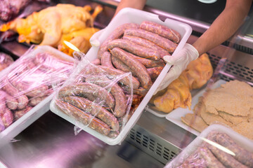 Close-up view of plastic container with sausages held in hands by seller against background of...