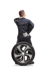 Fototapeta premium Rear view of a car mechanic in a uniform sitting on a tire and holding painful back