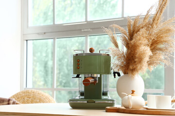 Modern coffee machine, vase with pampas grass and cups on table in kitchen