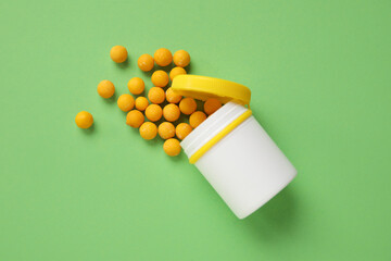 Jar with scattered pills on green background