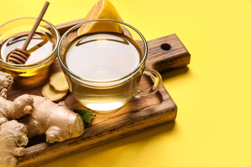 Glass cup of ginger tea and bowl with honey on yellow background