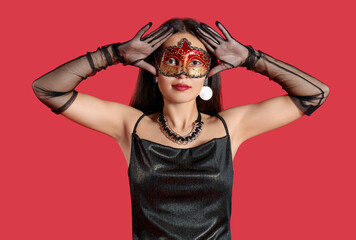 Beautiful young Asian woman in carnival mask on red background