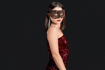 Beautiful young woman in carnival mask on black background