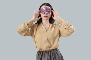Beautiful young woman in carnival mask on grey background
