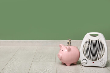 Electric fan heater and piggy bank on floor. Heating season