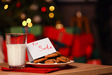 Naklejka na ściany i meble Paper with text FOR SANTA, Christmas cookies and milk on table at night, closeup