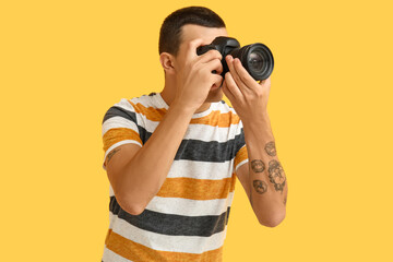 Male photographer with modern camera on yellow background