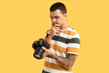 Thoughtful male photographer with modern camera on yellow background