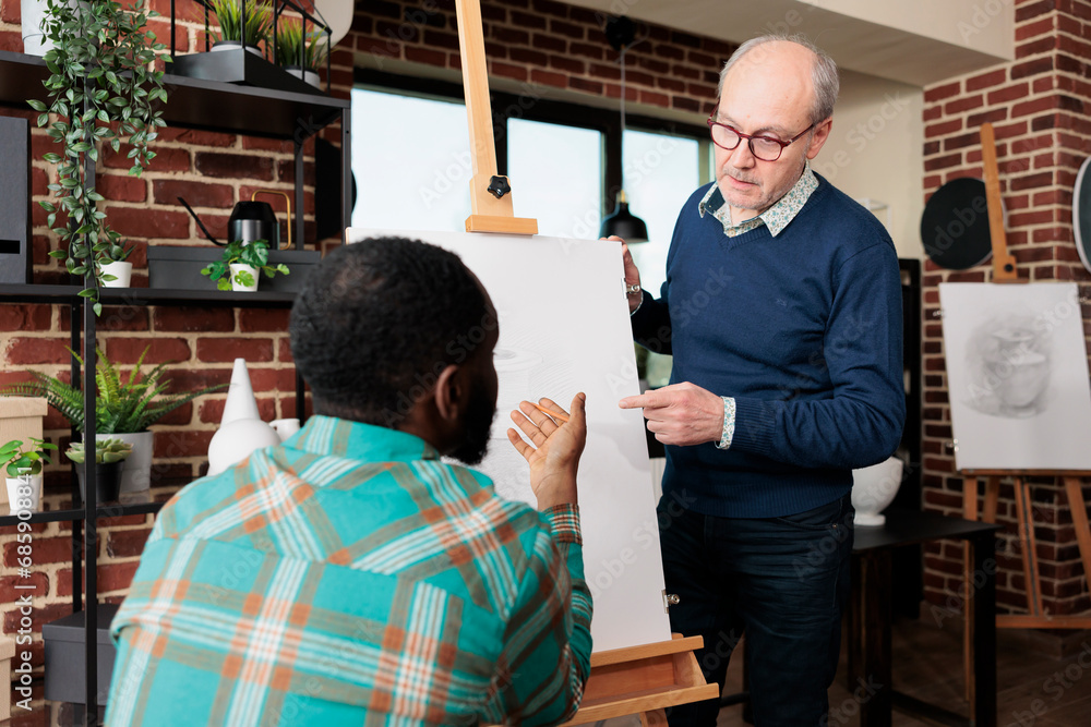 Poster people connecting while learning new skills, two diverse men looking at easel with canvas discussing