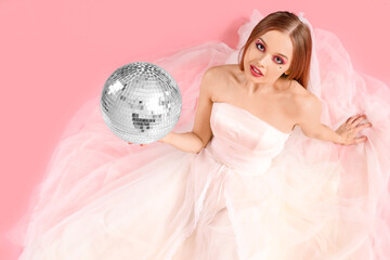 Beautiful young bride with disco ball sitting on pink background