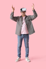 Happy young man using VR glasses on pink background