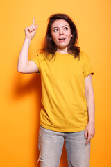 Positive woman standing over isolated orange background with index finger pointing up. In studio, Caucasian female adult having a great idea while gesturing and looking upwards.