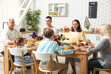 Happy family praying before dinner at festive table on Thanksgiving Day