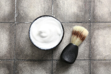 Bowl of shaving foam with brush on grunge grey tile background