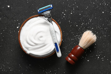 Bowl of shaving foam with brush and razor on grunge black background