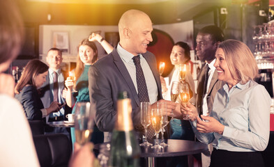 Glad positive smiling middle aged woman with male colleague enjoying office party in bar, talking...