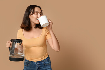 Beautiful young man with modern electric kettle drinking coffee on beige background