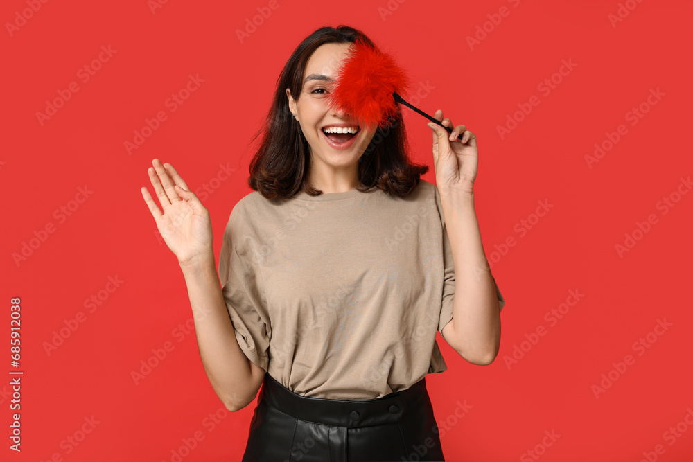 Wall mural Beautiful young woman with feather stick waving hand on red background