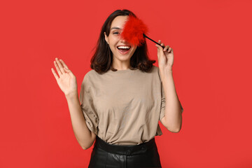 Beautiful young woman with feather stick waving hand on red background