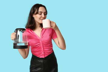 Beautiful young woman with modern electric kettle drinking coffee on blue background